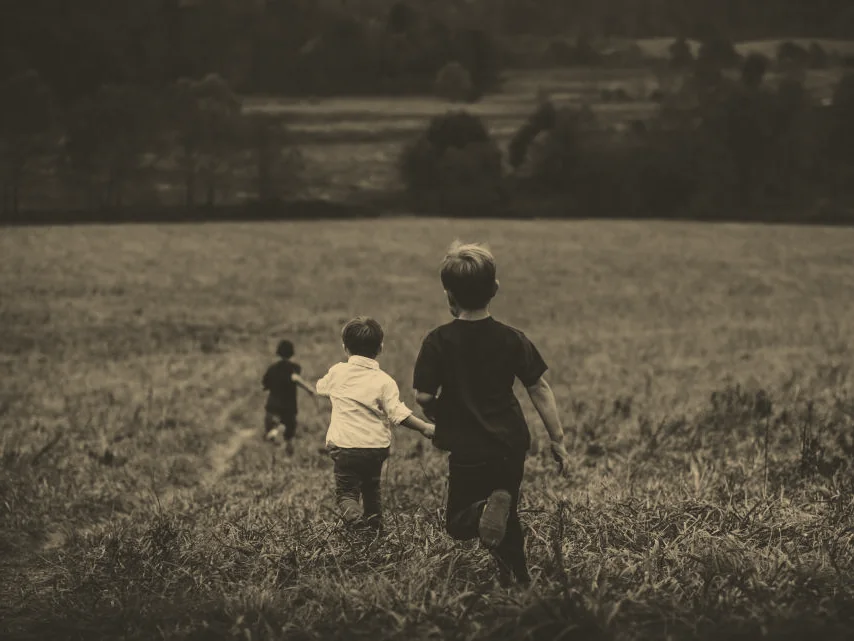 Trois enfants courant dans un champ, vus de dos